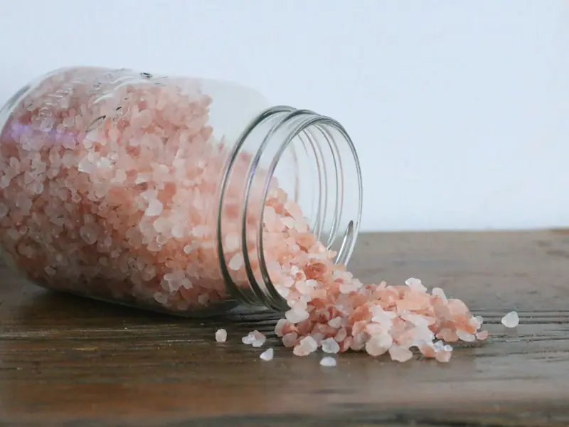 Bocal de sel rose renversé sur une table en bois