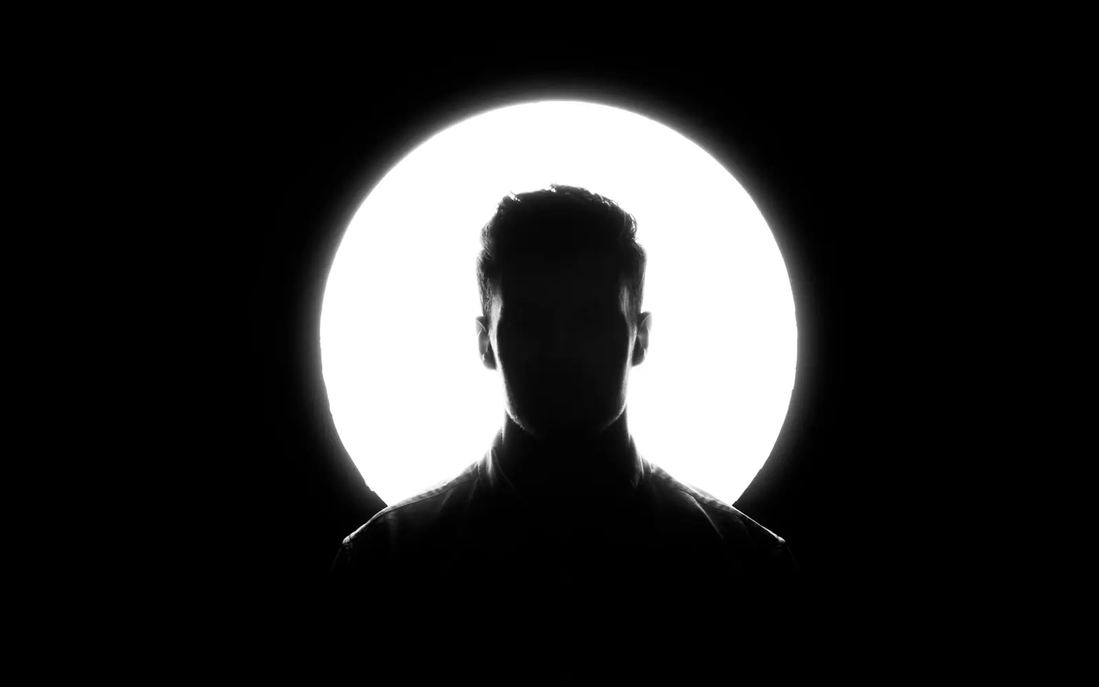 Silhouette en contre-jour devant un cercle de lumière, en noir et blanc